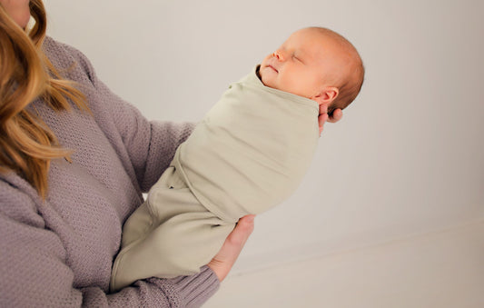 New mother lovingly holding her newborn wrapped in a LullaBaby swaddle, symbolizing the journey of postpartum health