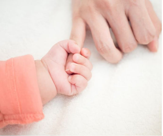 Newborn baby gently holding mother's hand, symbolizing LullaBaby's support for postpartum mental health and wellbeing for new mothers